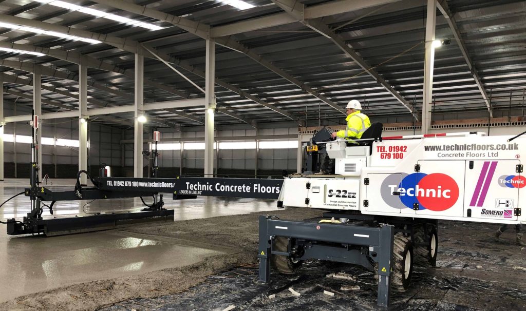 Somero laser screed machine placing a large industrial concrete floor inside a steel framed warehouse